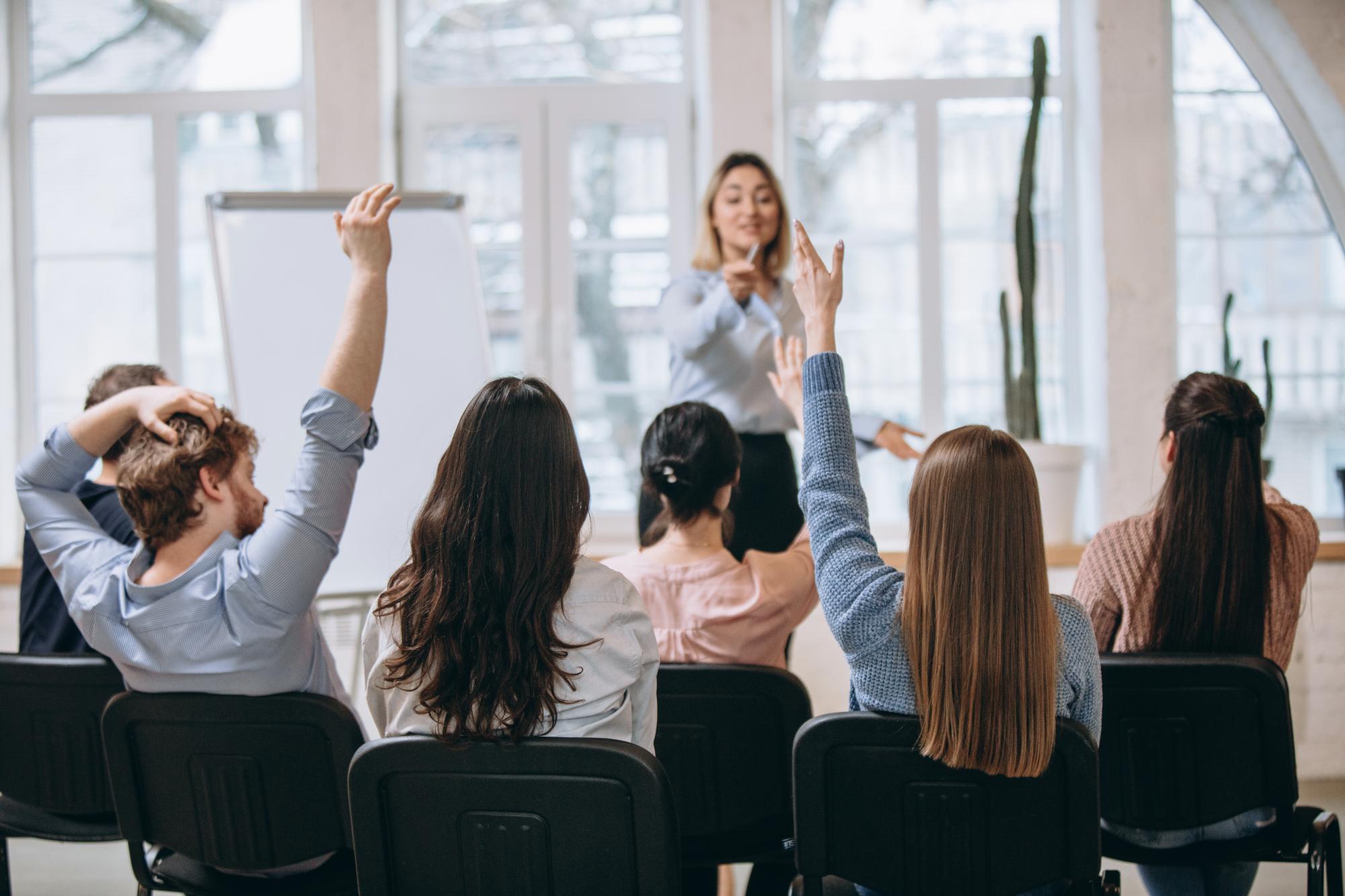 Zdjęcie poglądowe przedstawiające kobietę prowadzącą zajęcia i grupę studentów.