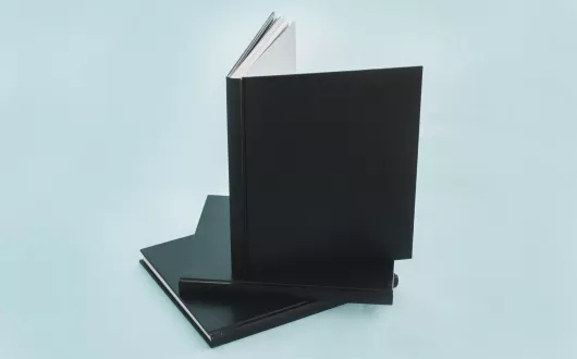 Książka w czarnej skórzanej oprawie stoi na dwóch takich samych jak ona książkach.