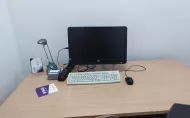 The interior of a room for individual study. Desk top with lamp, writing utensils and computer set on it. Part of the window and two chairs can be seen.