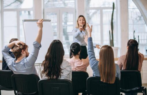 Zdjęcie poglądowe przedstawiające kobietę prowadzącą zajęcia i grupę studentów.