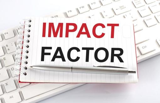 Zdjęcie poglądowe przedstawiające notatnik z napisem Impact Factor, położony na klawiaturze komputera.