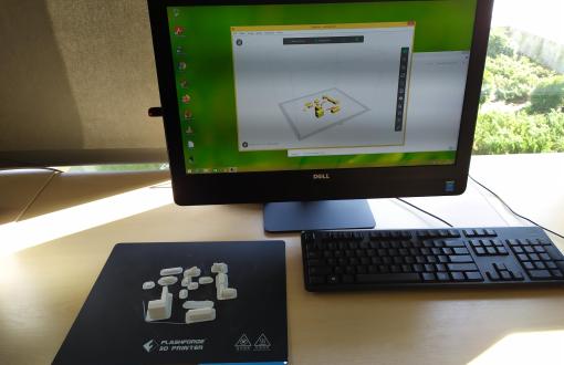 Zdjęcie przedstawiające ekran monitora z widocznymi planami budynków, obok klawiatury znajdują się wydrukowane w 3D miniaturowe budynki.