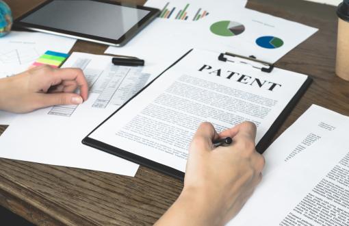Kobiece dłoń podpisuje dokument zatytułowany Patent