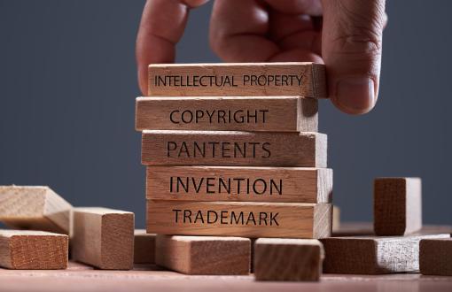 dłoń układająca drewniane klocki z napisami:Intellectual property, Copyright, Patents, Invention, Trademark